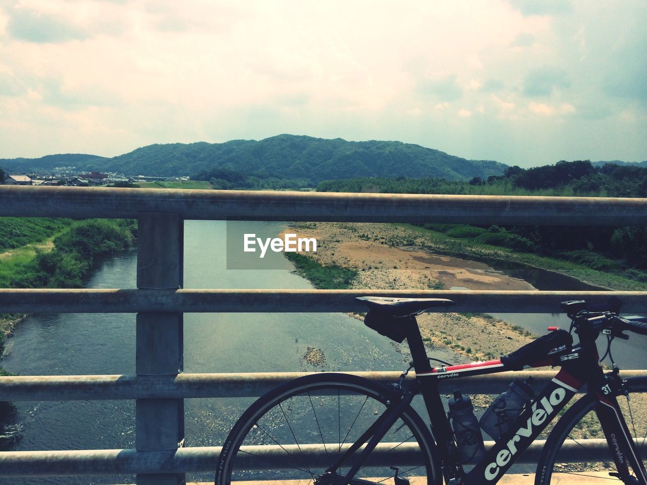 Bicycle parked on bridge over river against cloudy sky during sunny day