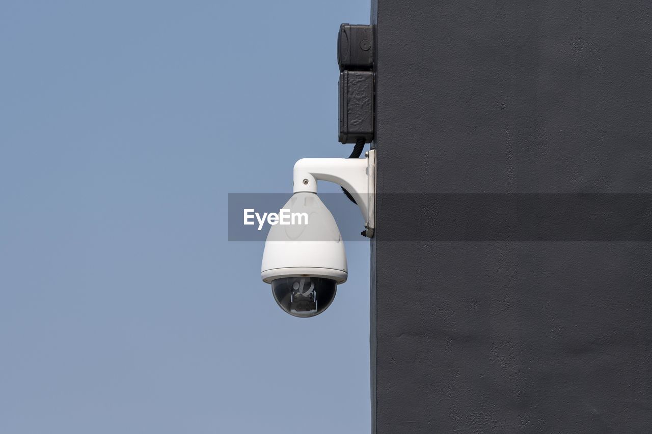 Low angle view of security camera on building against clear blue sky during sunny day