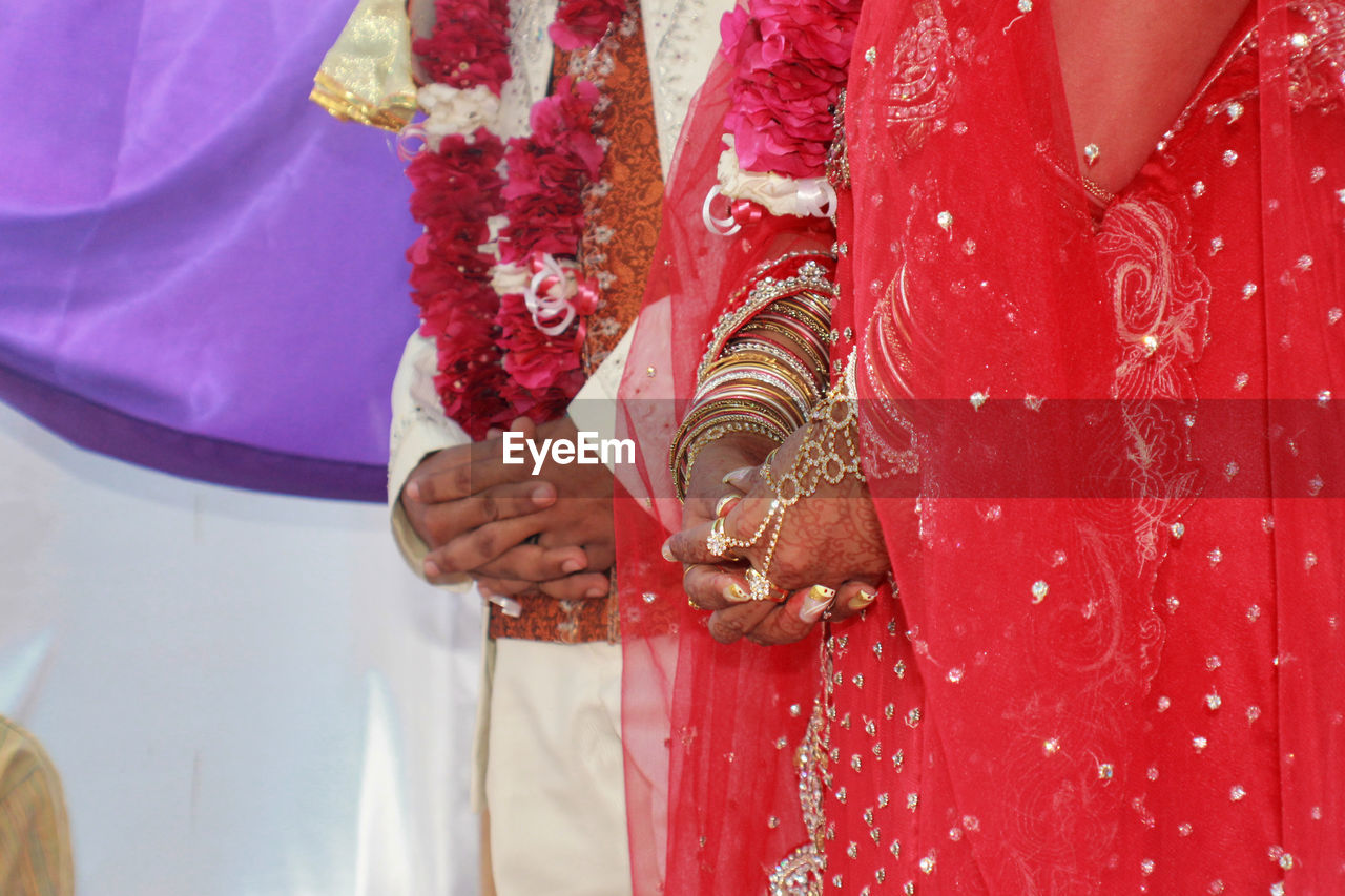 Midsection of bride and groom with hands clasped during ceremony