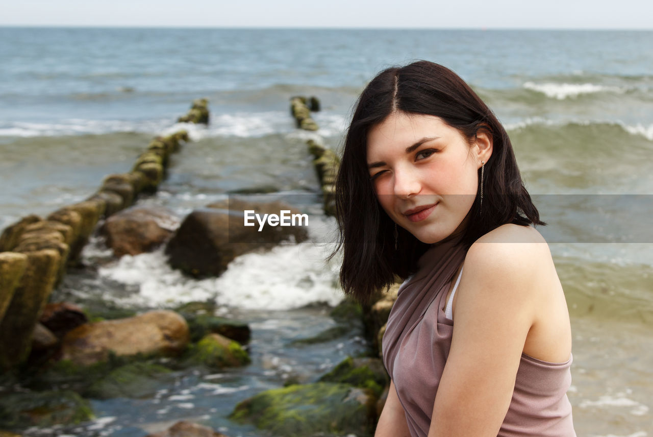 Portrait of beautiful young woman sitting by sea