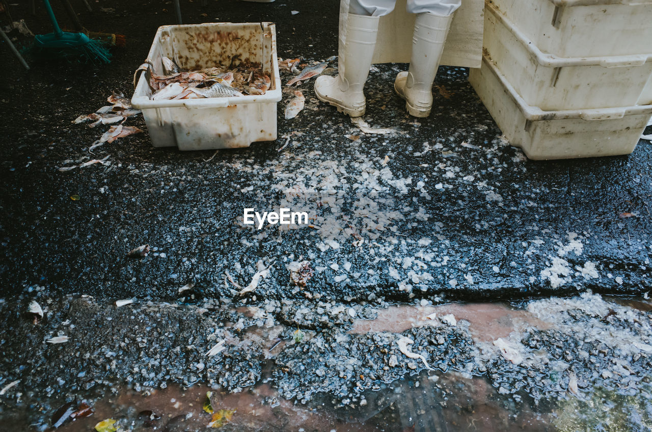 Low section of working man standing on wet ground with fish scraps around him