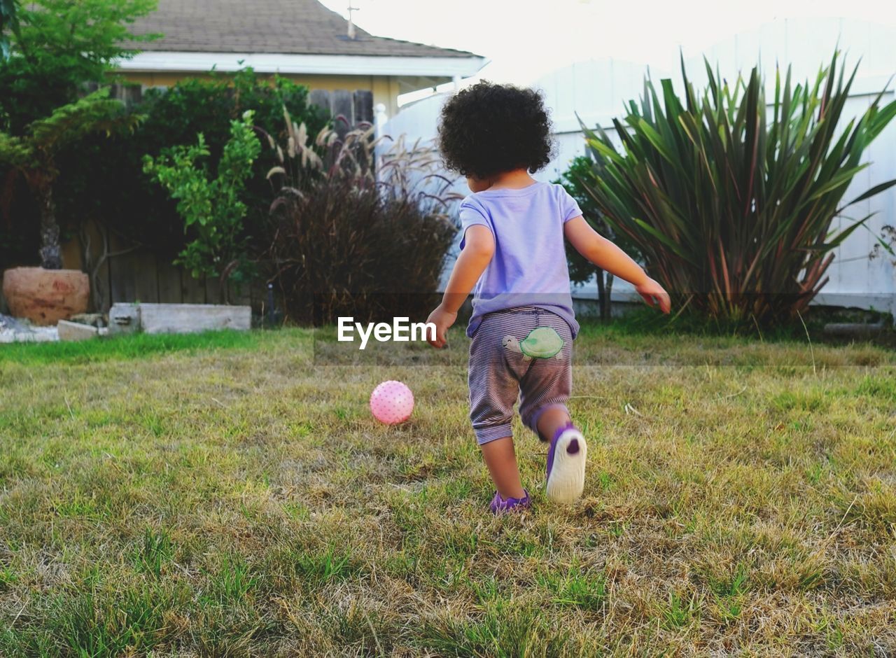 Rear view of boy playing with ball while running on grassy field