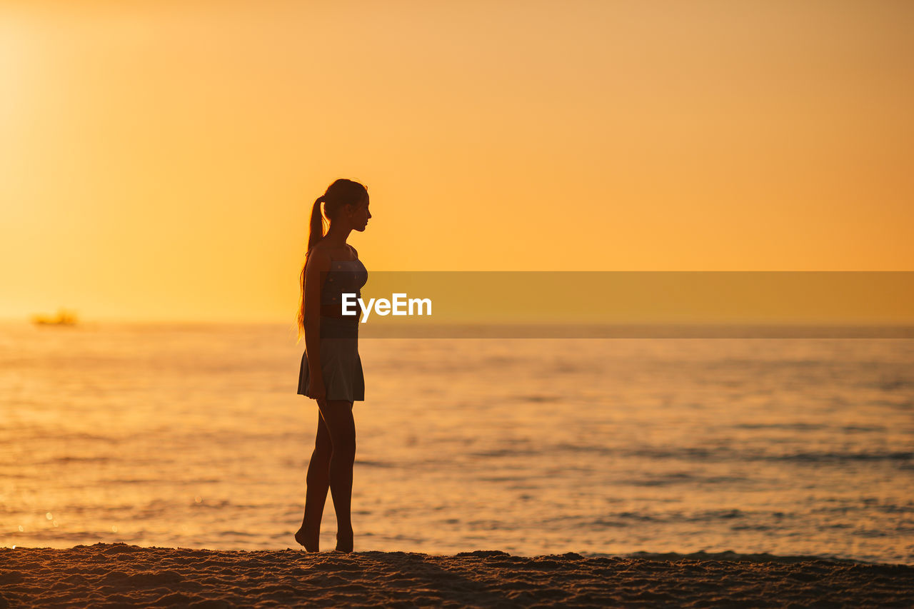 silhouette woman standing on beach against sky during sunset