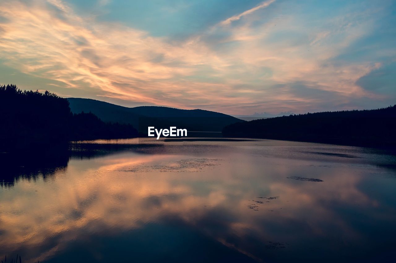 Scenic view of lake by silhouette mountains against sky during sunset