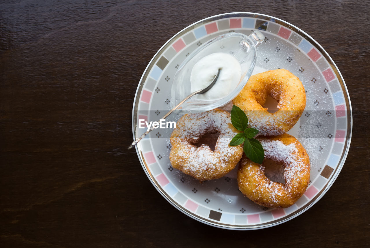 Three tasty donuts with powdered sugar, mint leaf and sour cream on plate. dark wooden background .