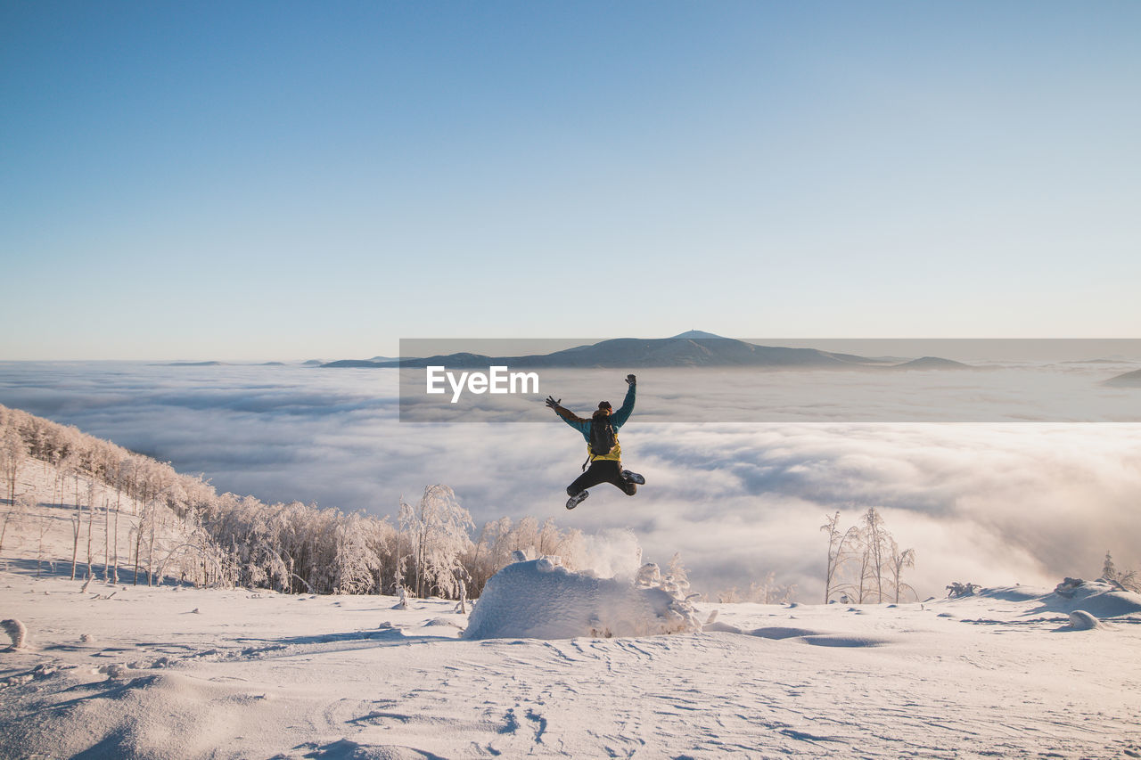 Energetic boy in winter clothes jumping from a stump into the fresh snow with a view of the sunrise