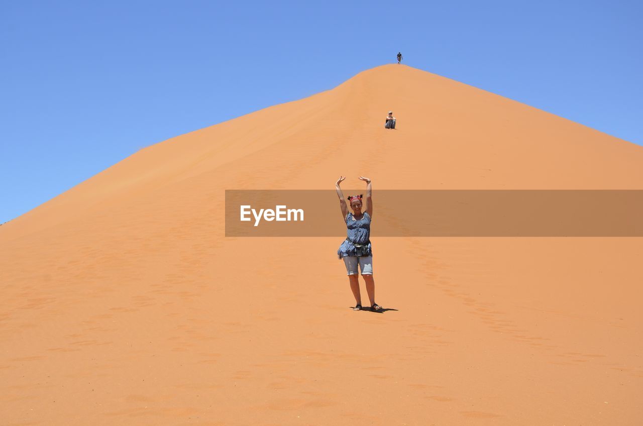 FULL LENGTH OF YOUNG WOMAN STANDING ON SAND DUNE