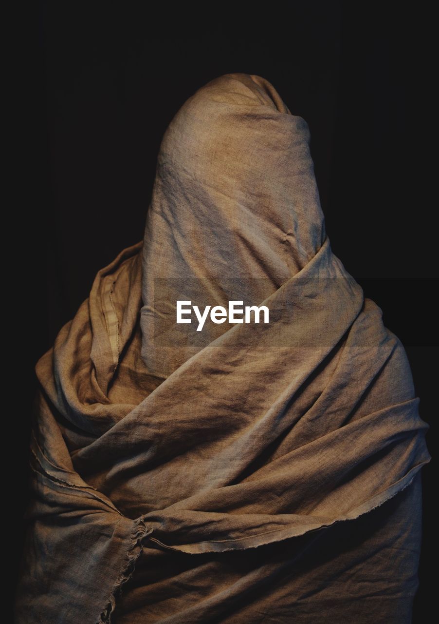 Person covered with fabric standing against black background