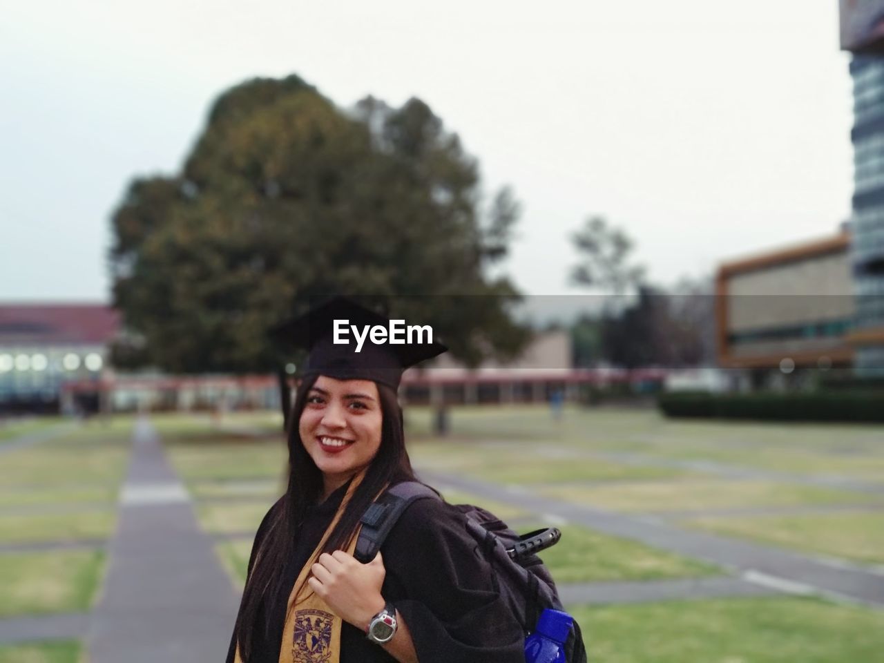 Smiling woman in graduation gown standing on field campus