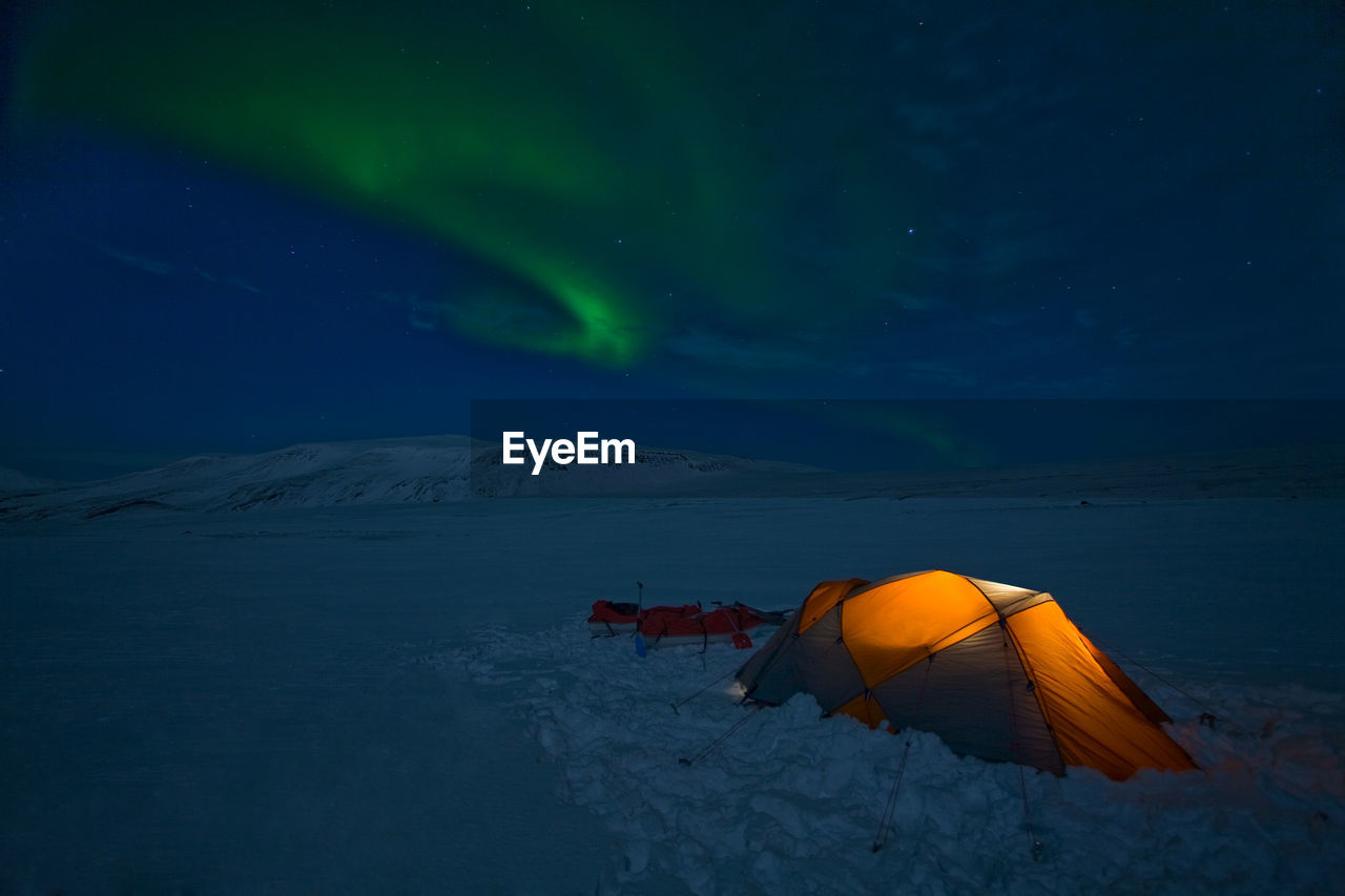 Aurora borealis over an illuminated tent on langjokull glacier