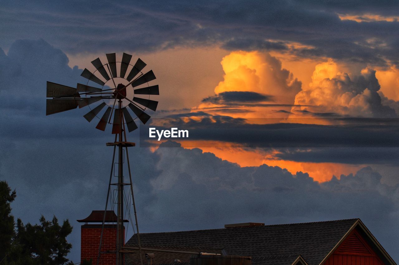Traditional windmill by buildings against sky during sunset