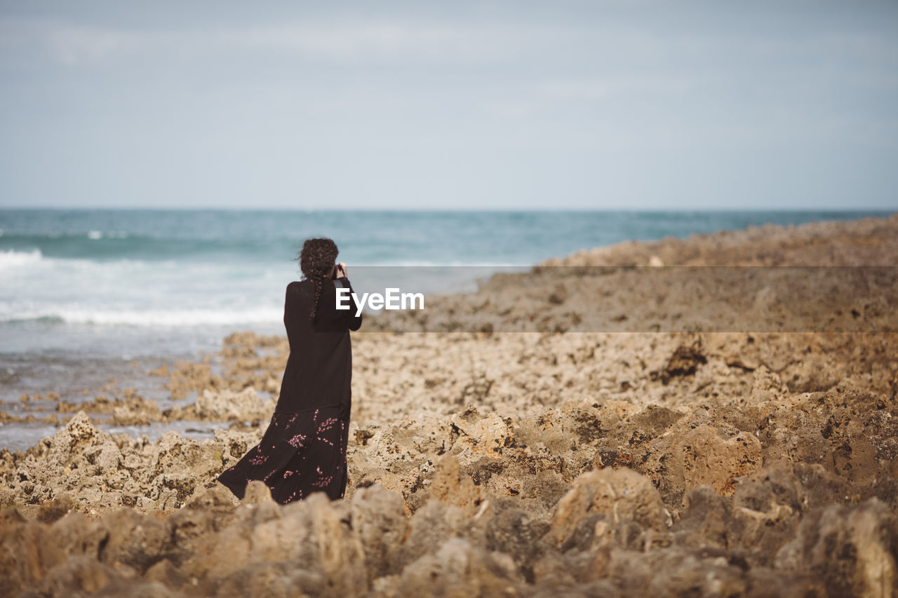 Rear view of woman photographing on beach 