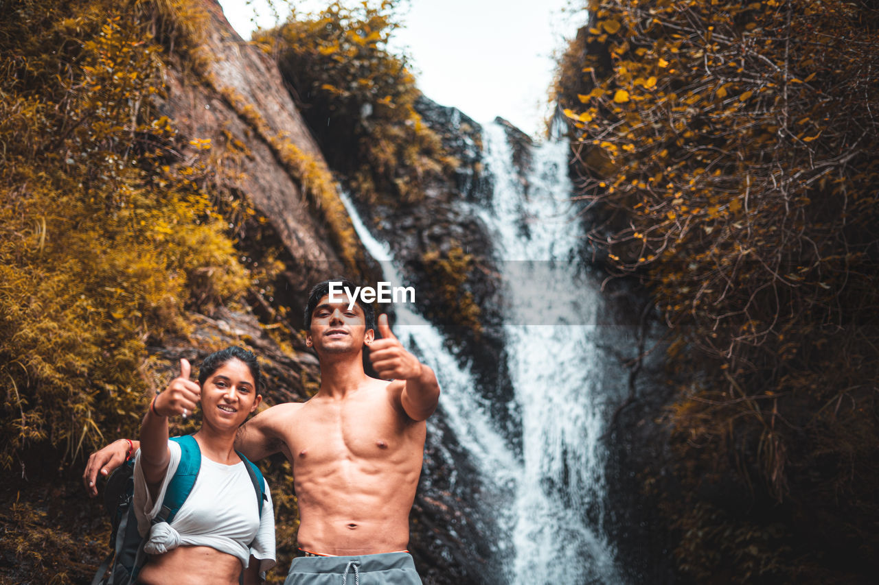 Young couple enjoying the beautiful waterfall view and showing thumbs up in the camera.