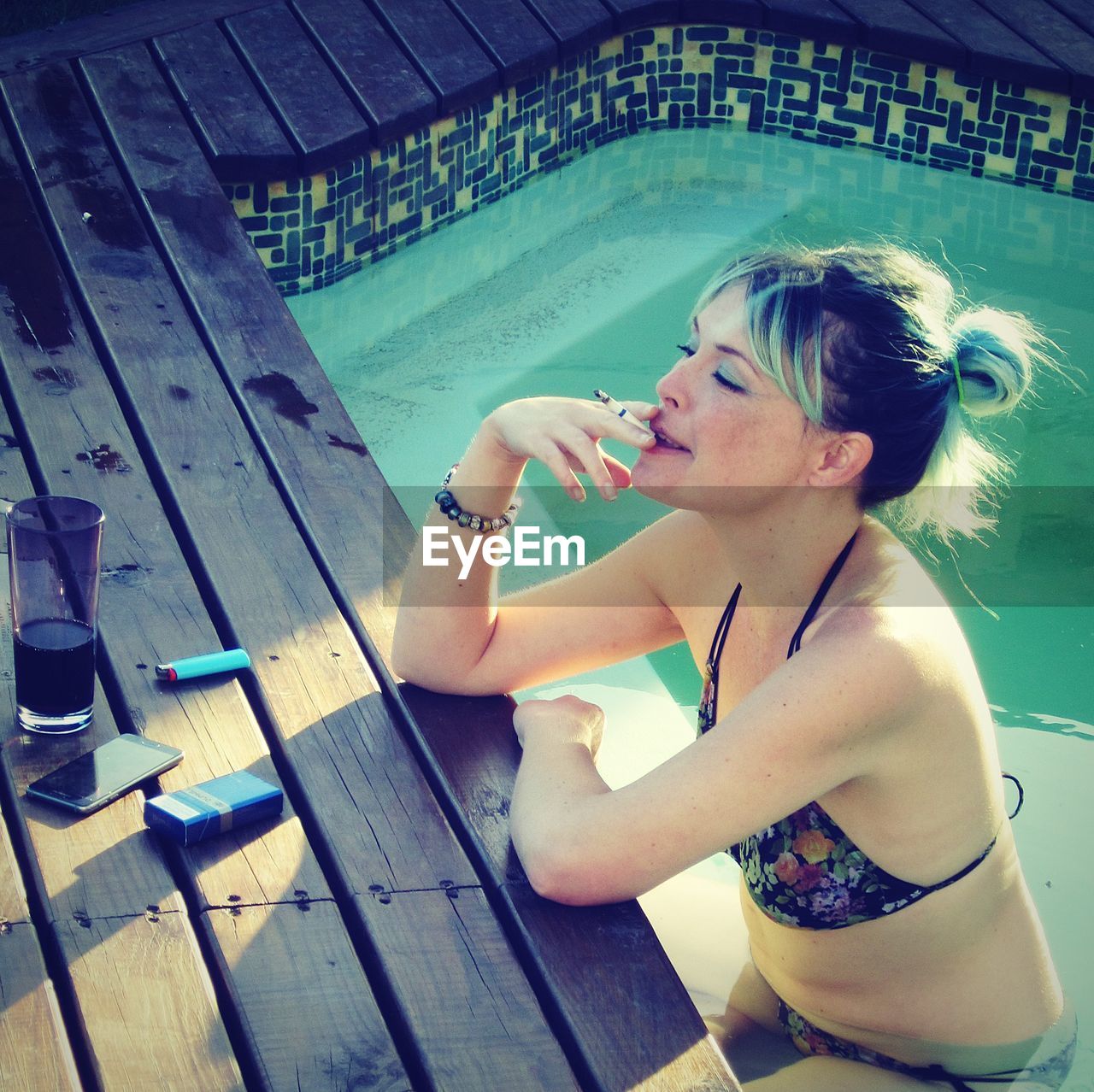 High angle view of woman smoking cigarette while sitting in swimming pool