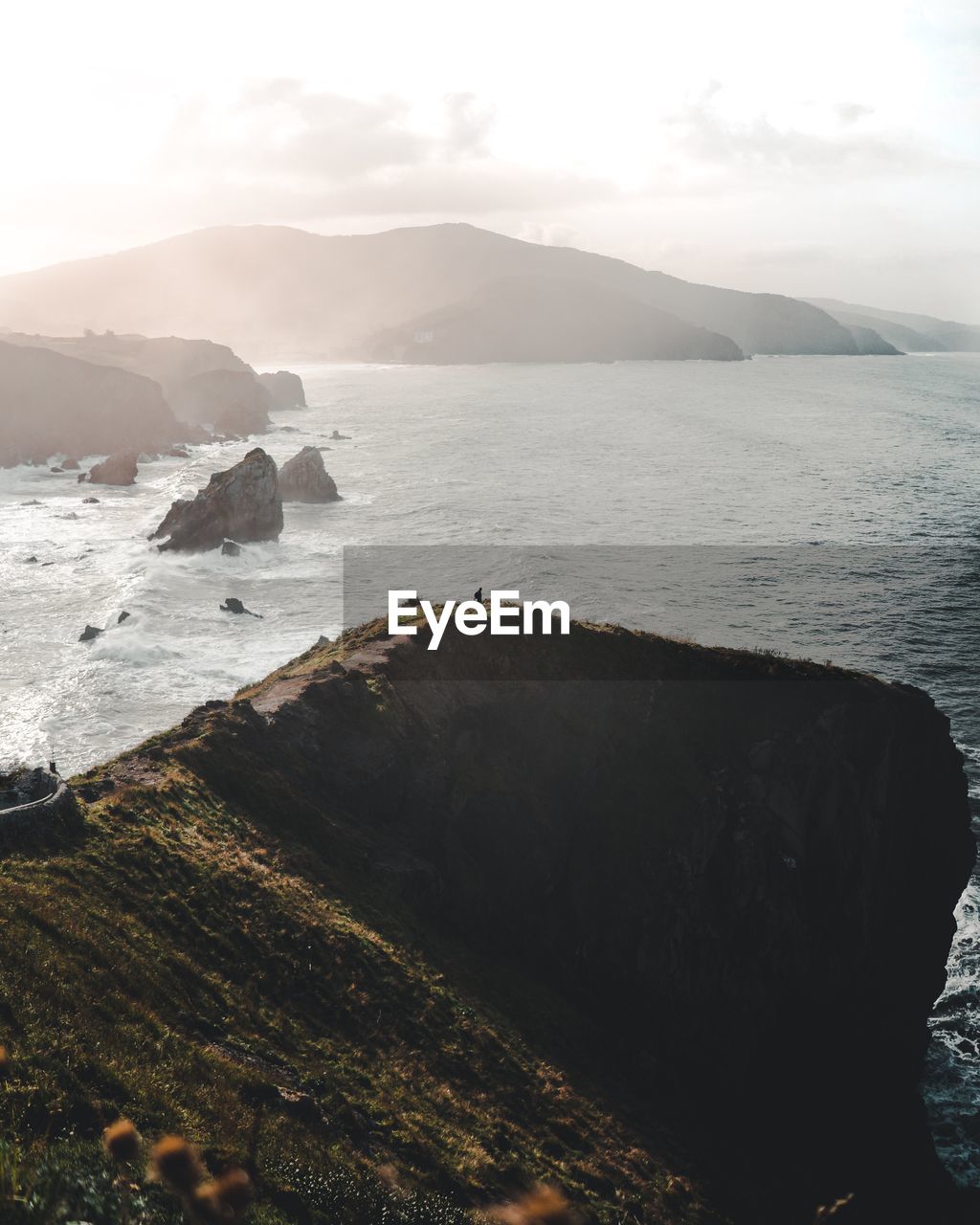 Scenic view of sea and rocky coastline with mountain against sky