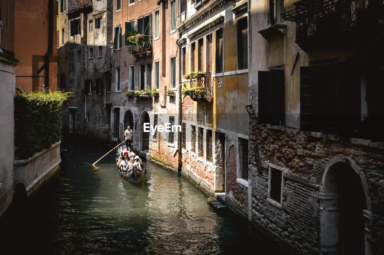 PEOPLE ON CANAL AMIDST BUILDINGS IN CITY