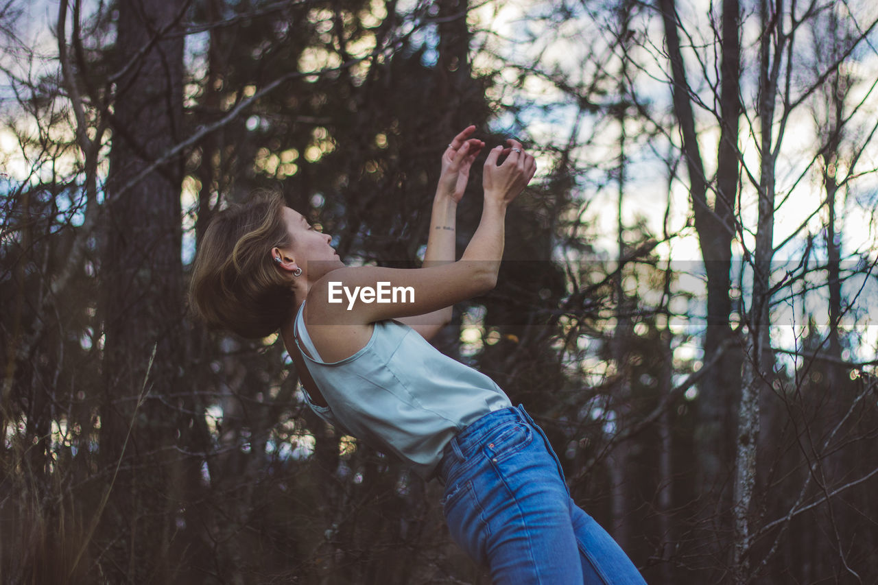 Side view of young woman dancing against trees in forest