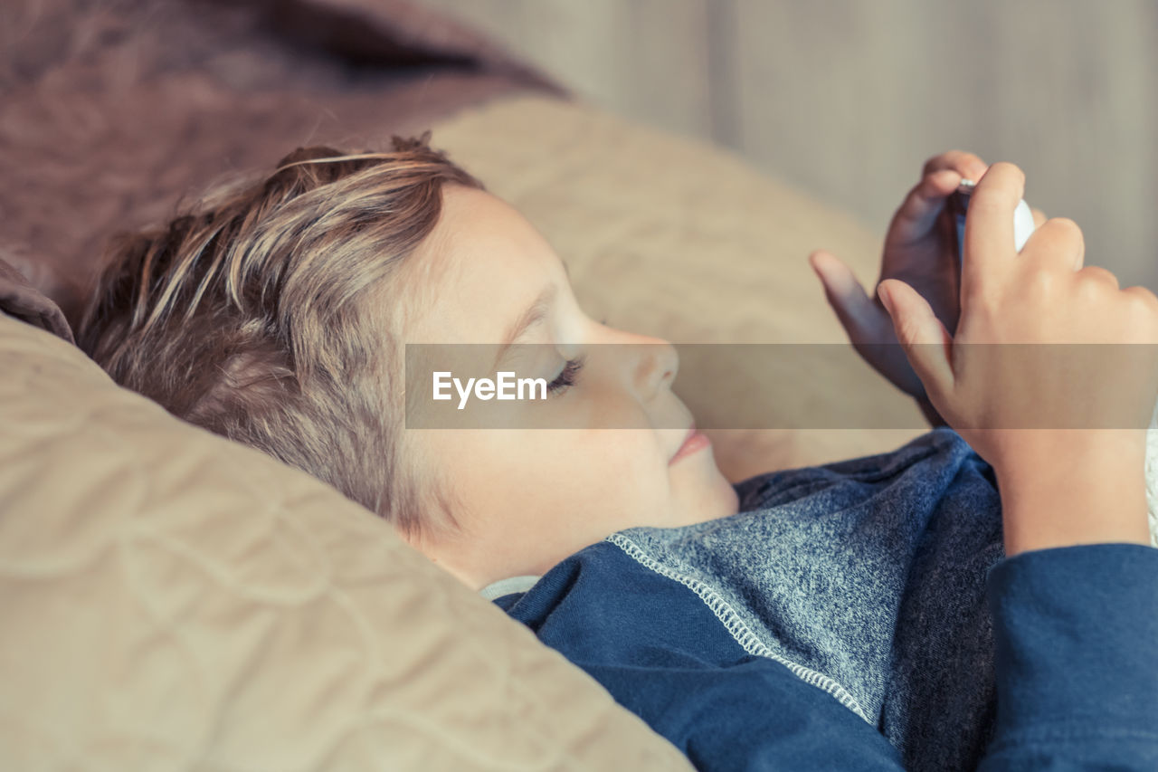 Side view of boy using mobile phone while lying on bed at home