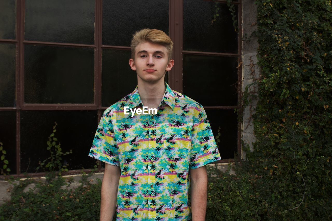 Portrait of young man standing against window