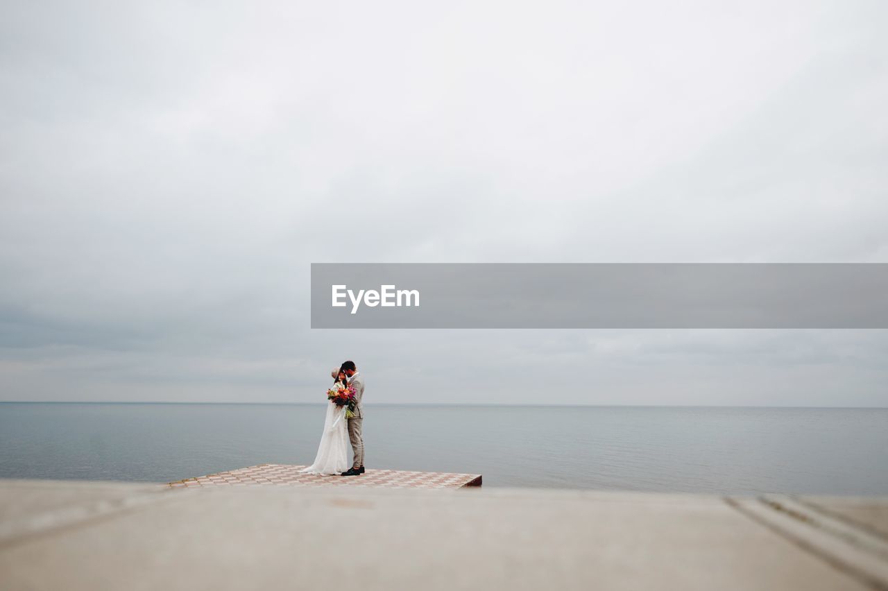Bride and bridegroom standing on pier in sea during wedding ceremony
