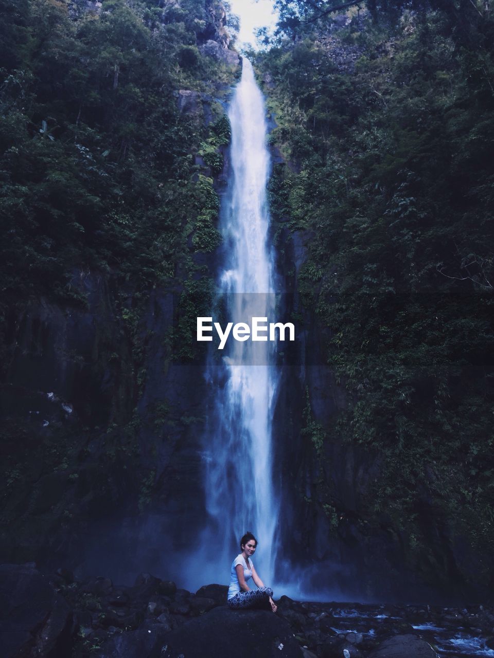 Woman sitting against waterfall in forest