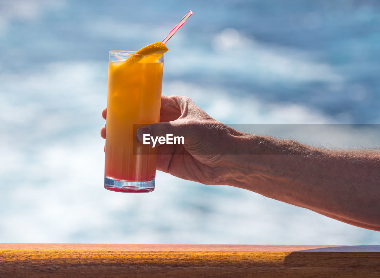 Cropped hand of man having drink on boat in sea