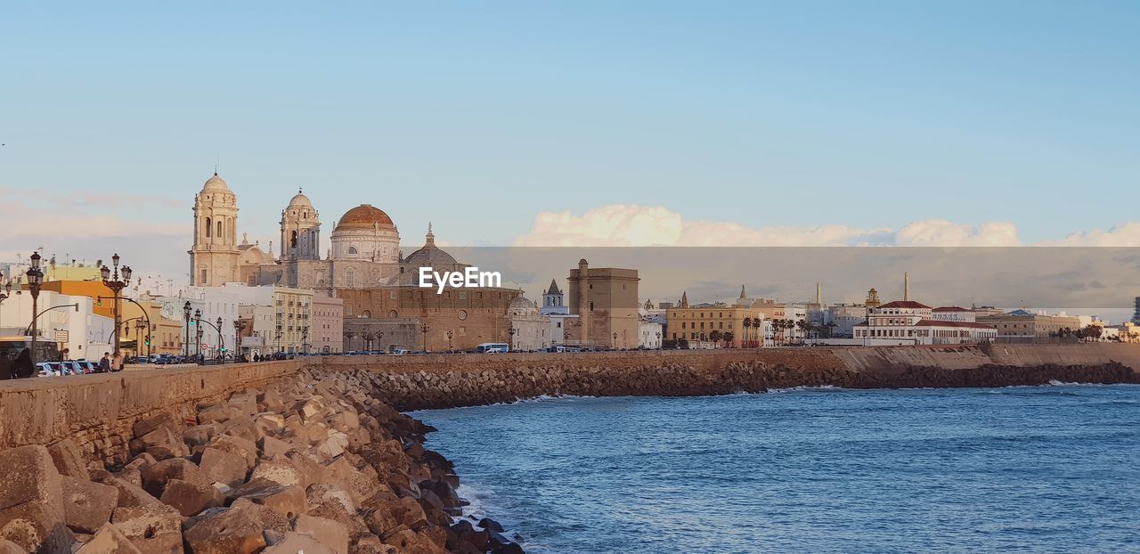 Historic buildings in city by sea against blue sky