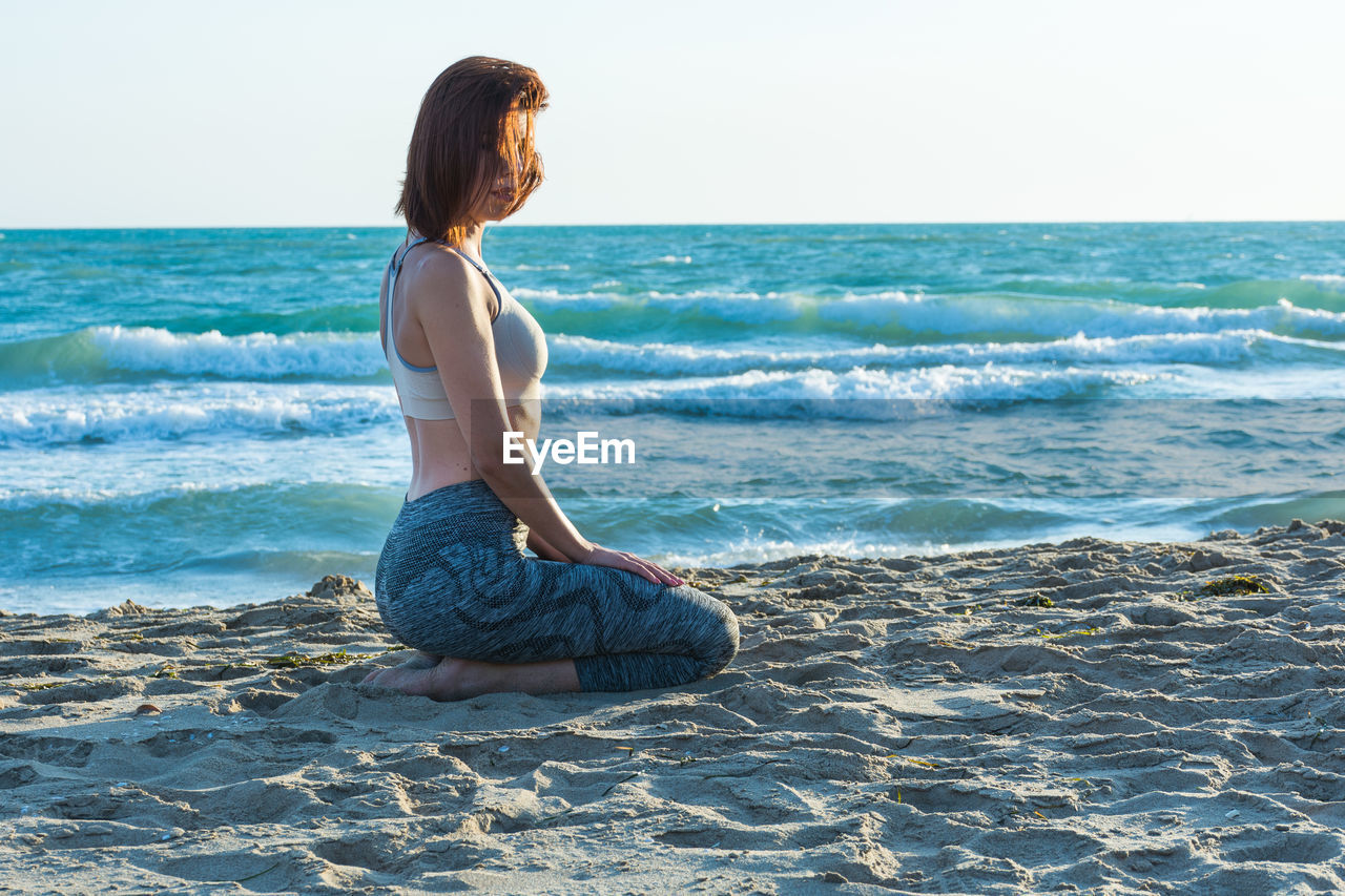Side view of young woman kneeling at beach