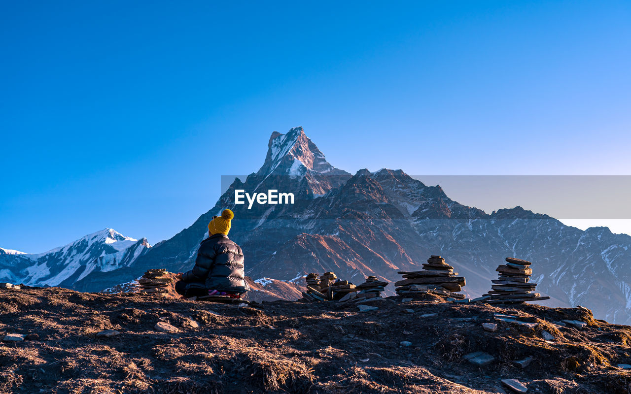 rear view of man walking on mountain against clear blue sky