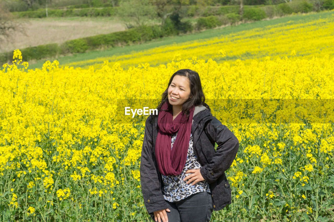 Smiling woman standing with hand on hip in oilseed rape field