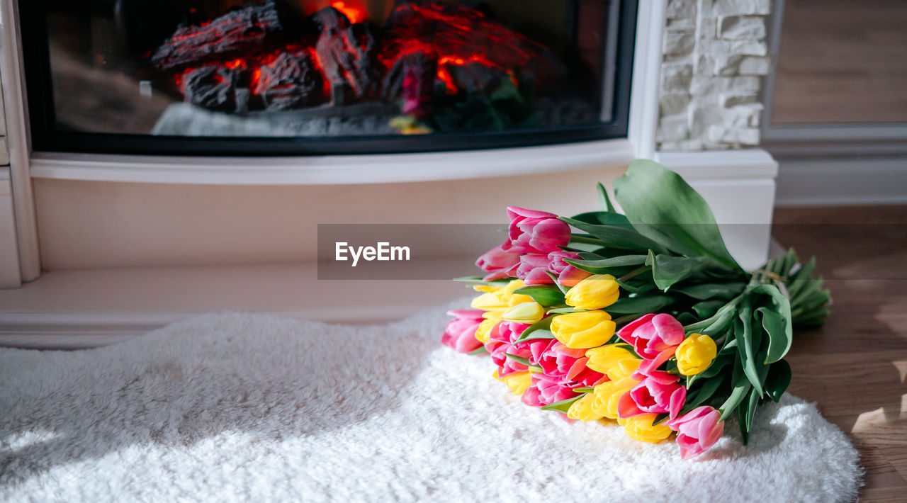 Fresh spring yellow and pink tulips bouquet on the fur carpet floor by the fireplace with copy space