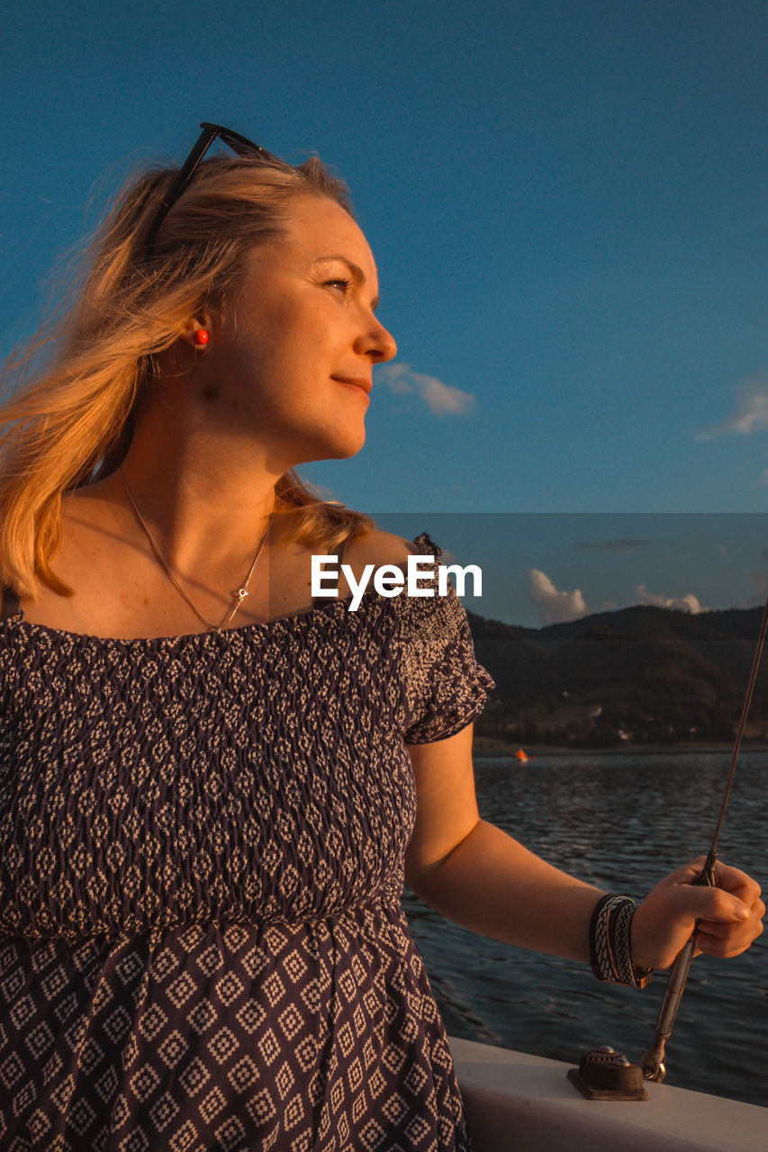 Mid adult woman looking away while standing in boat on sea against sky during sunset