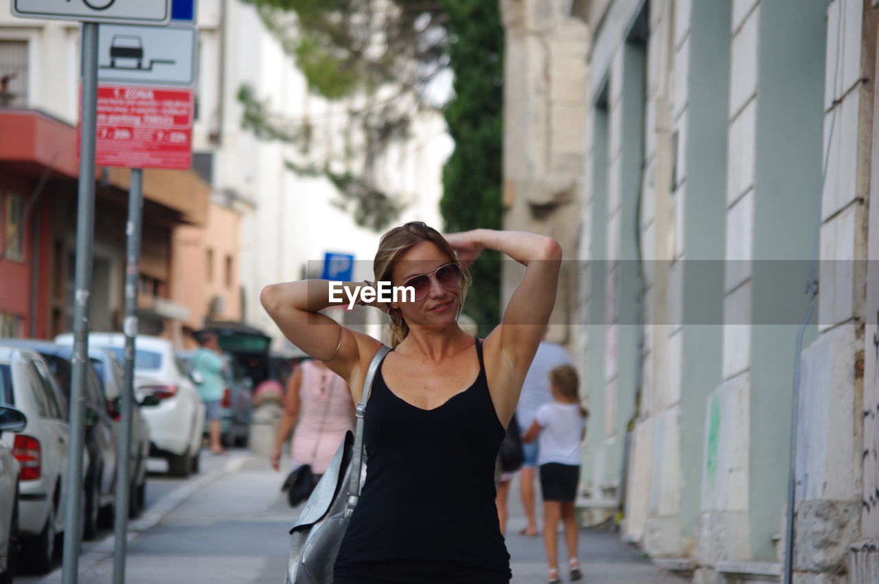 Portrait of woman standing on sidewalk in city