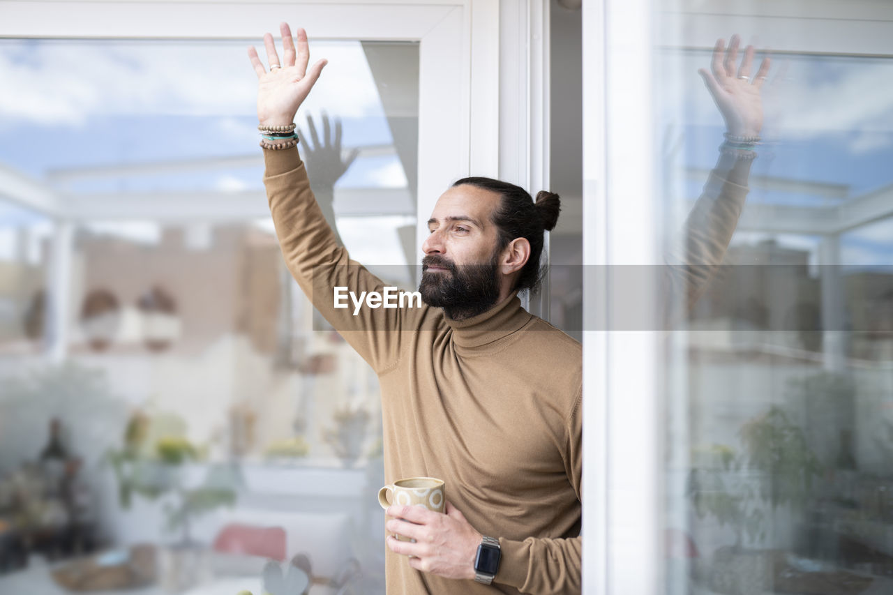 Handsome man waving while holding mug at doorway