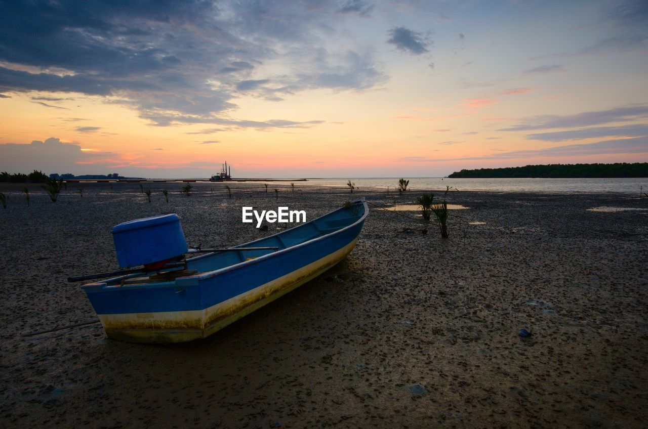 Boat moored on beach against sky during sunset