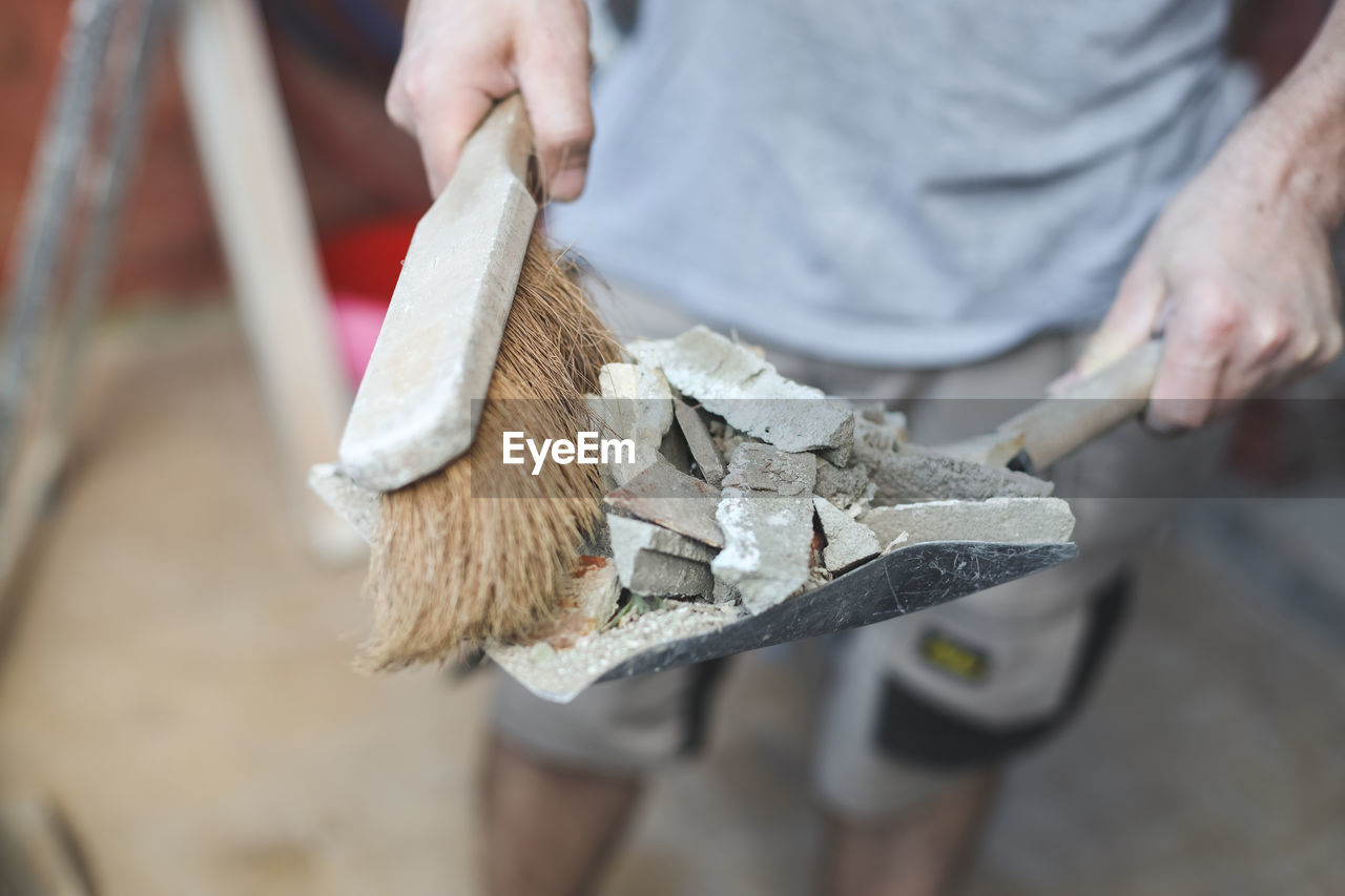 A young caucasian man holds a scoop with construction waste and a broom to throw it into a bag