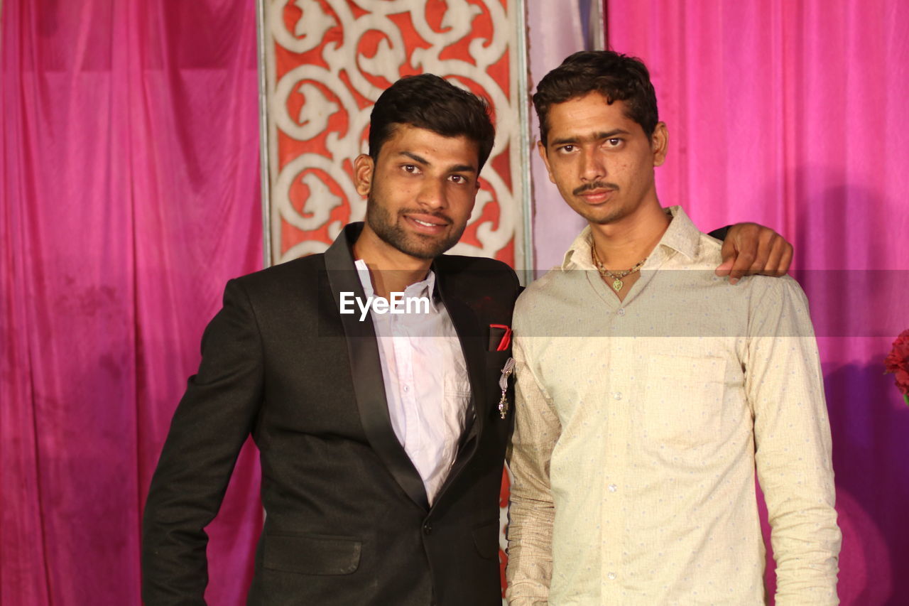 Portrait of brothers standing against curtain