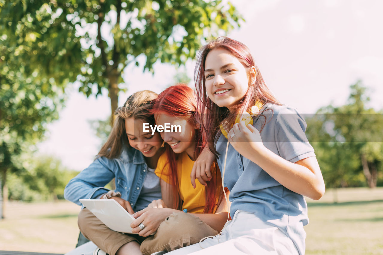 Attractive teenage girls are sitting on a park bench, discussing and smiling. 