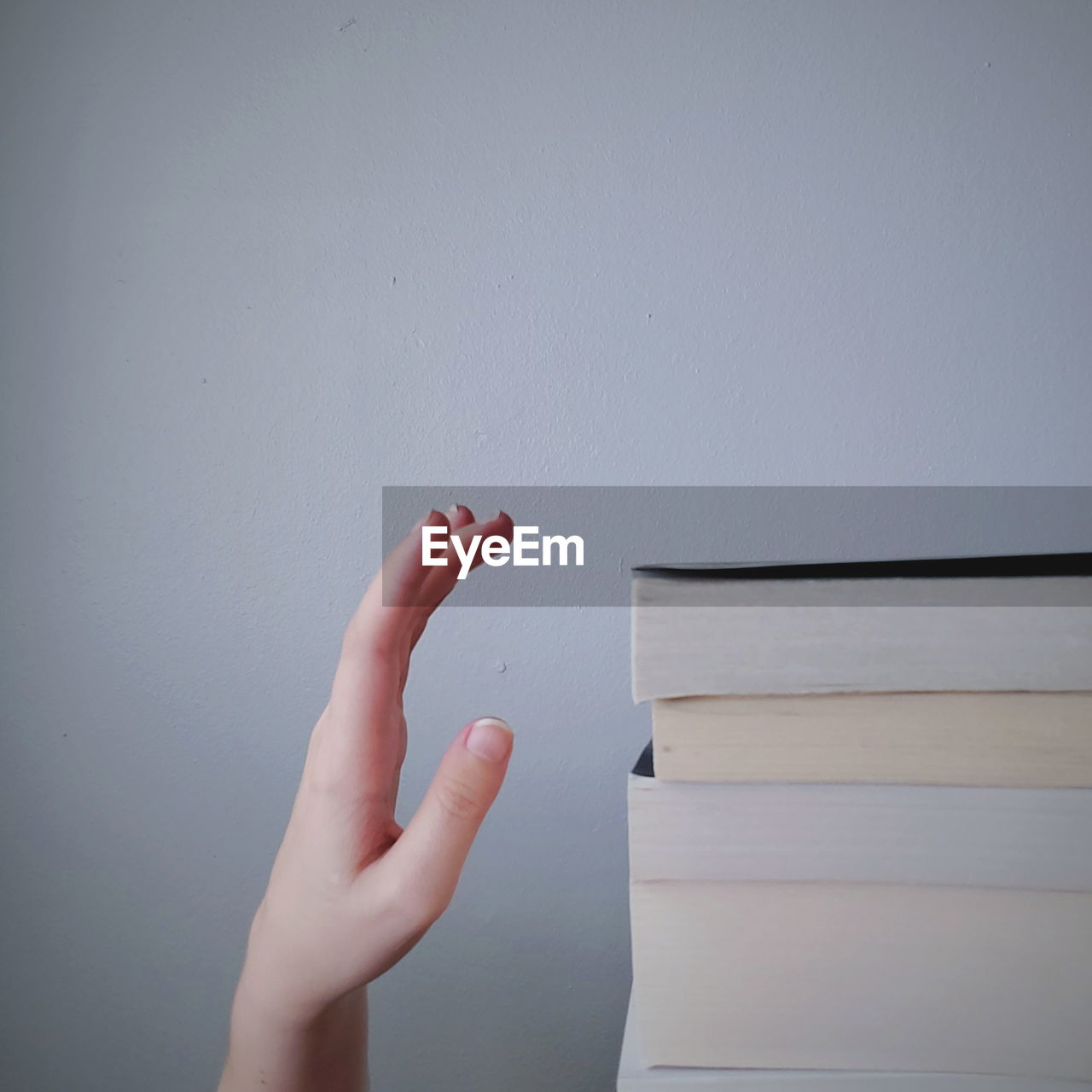 Cropped hand of person by book stack against wall