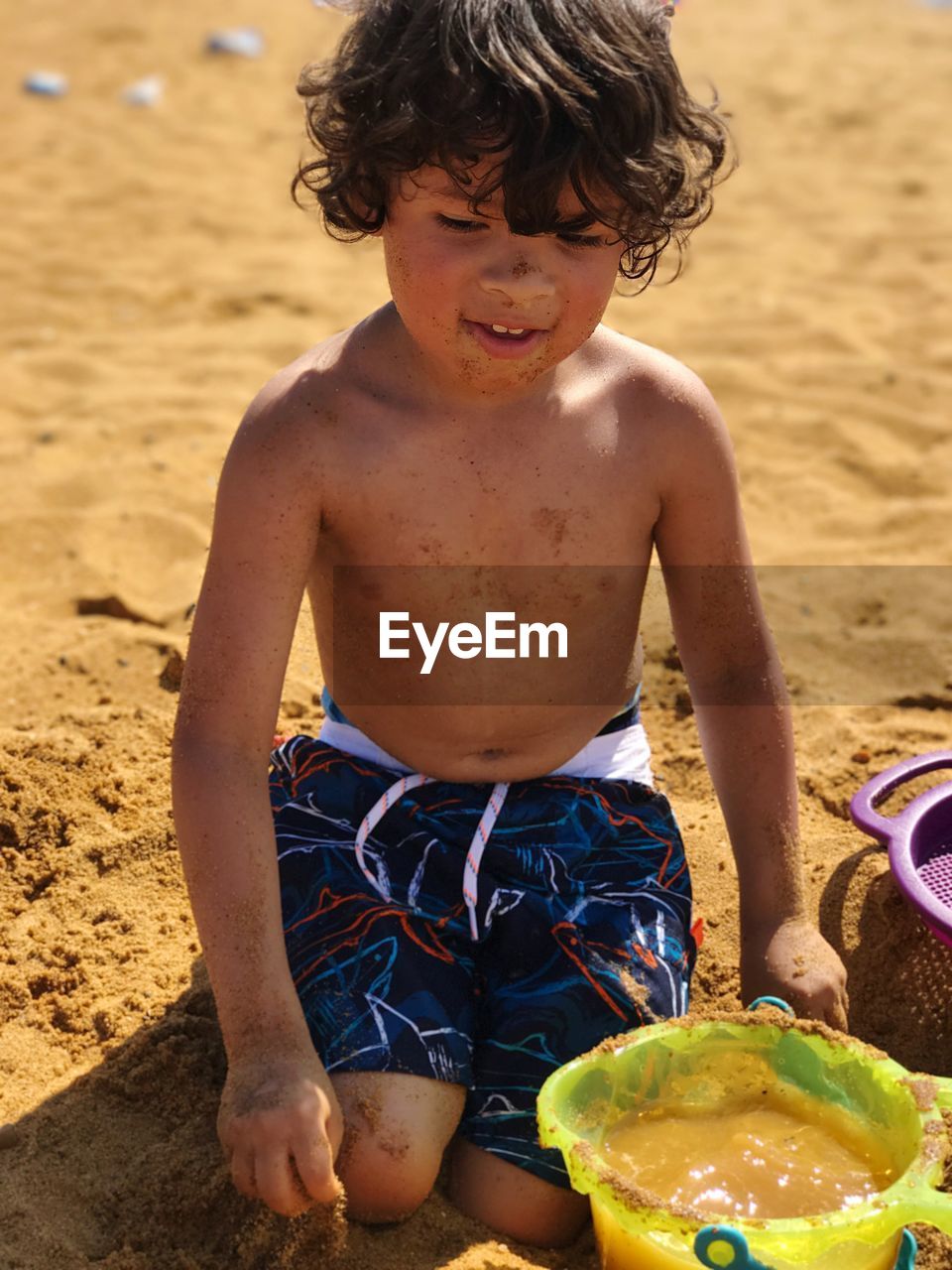 Playful shirtless boy with toys at sandy beach on sunny day