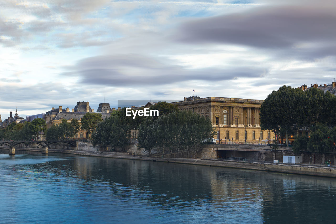 View of buildings by river against cloudy sky