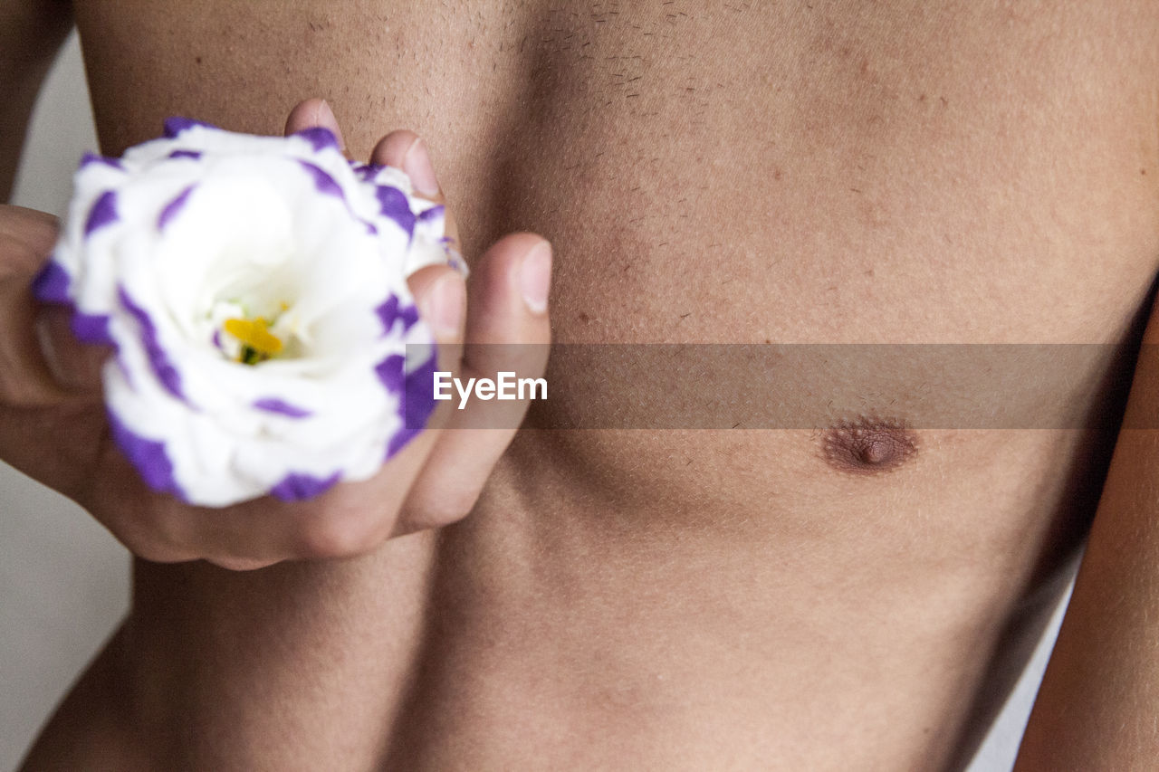 Midsection of shirtless man holding flower while lying on bed at home