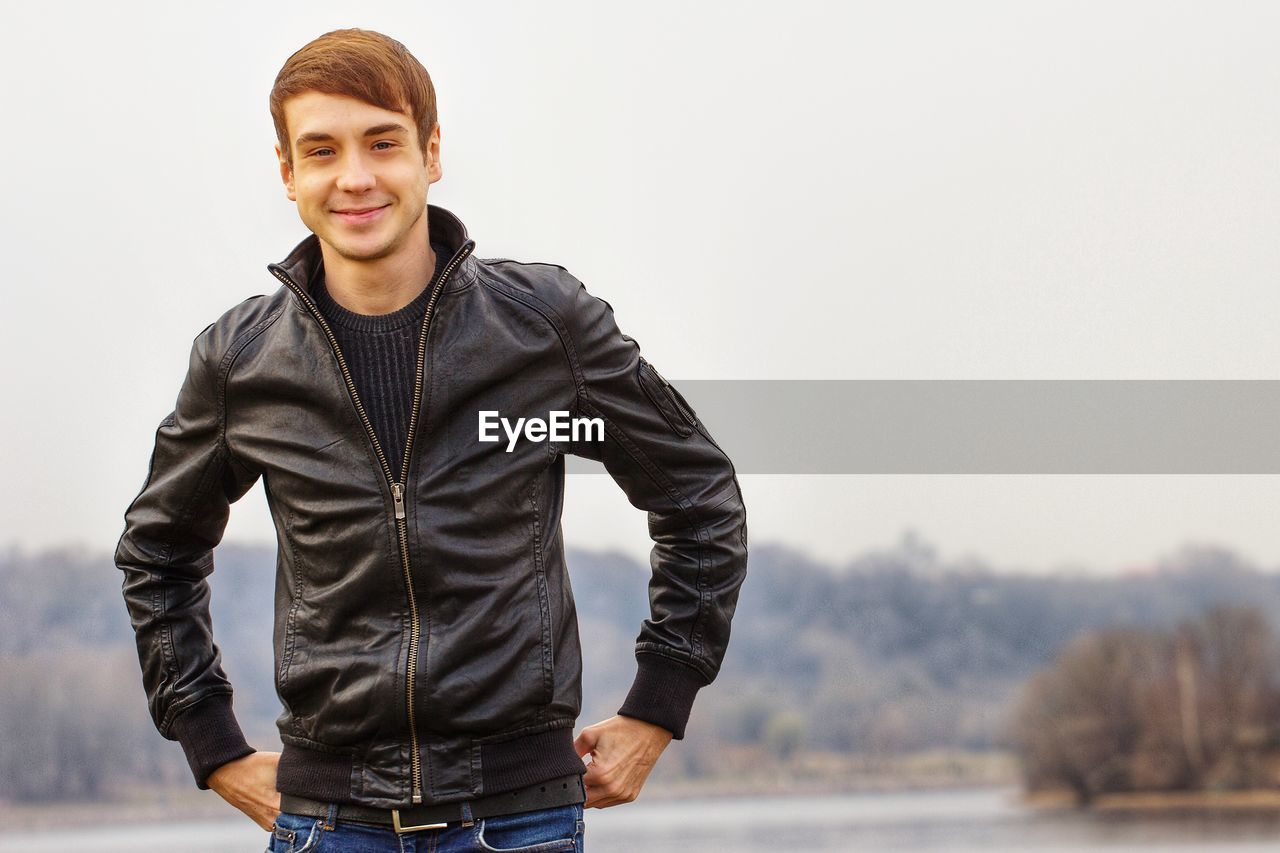 PORTRAIT OF YOUNG MAN STANDING AGAINST SKY