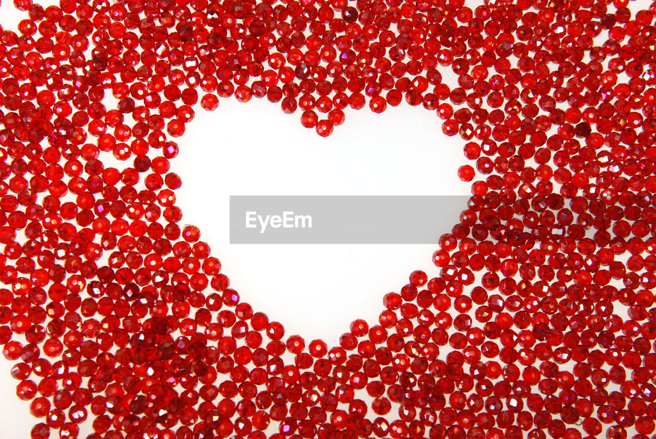 Close-up of heart shape made with beads against white background