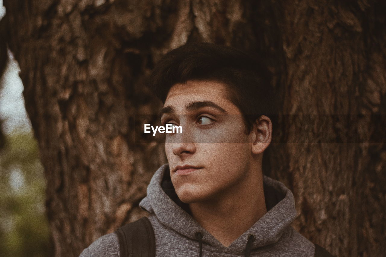 Young man looking away by trees