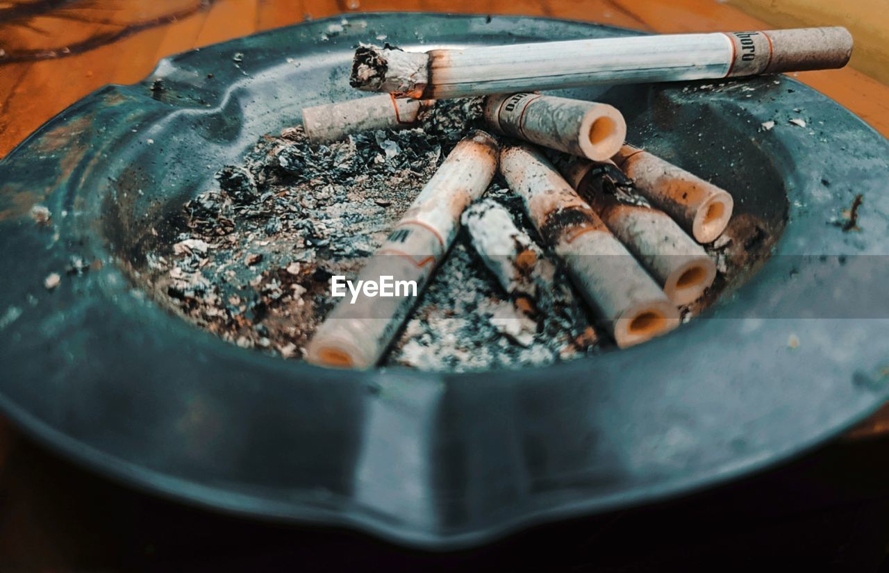 CLOSE-UP OF CIGARETTE SMOKING IN CONTAINER ON TABLE