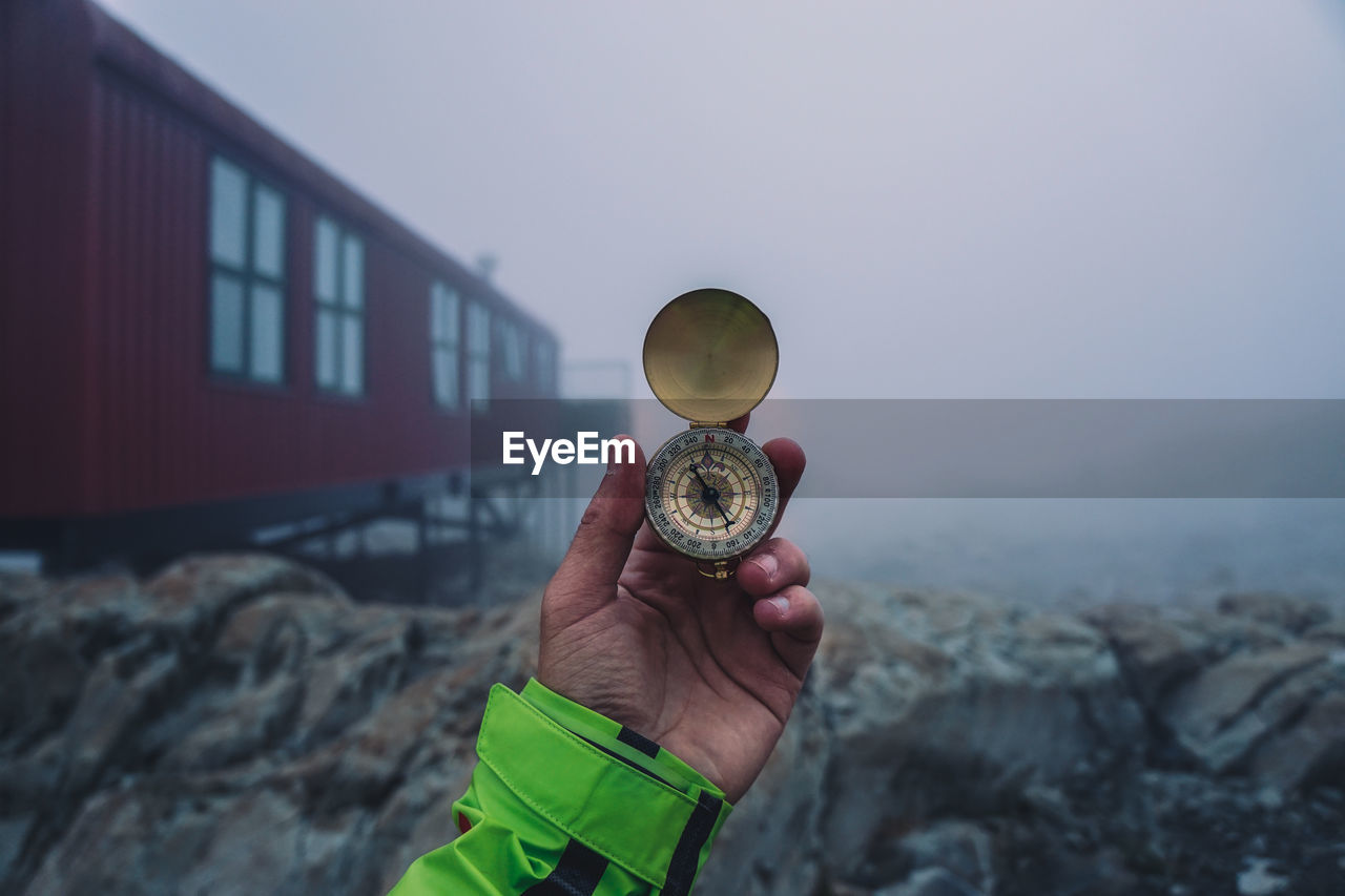 Close-up of hand holding navigational compass against sky