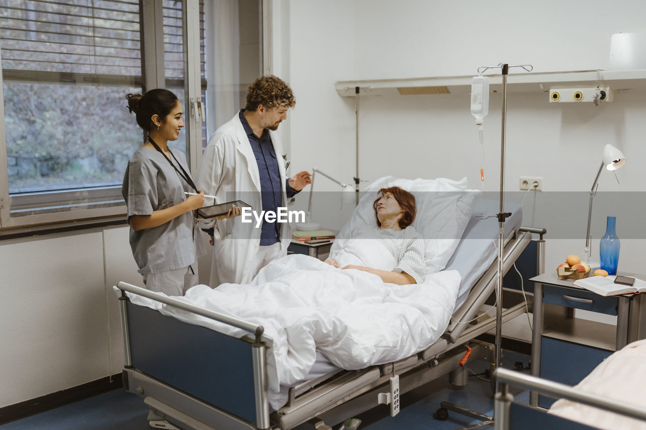 Healthcare workers talking to senior female patient lying on bed in hospital