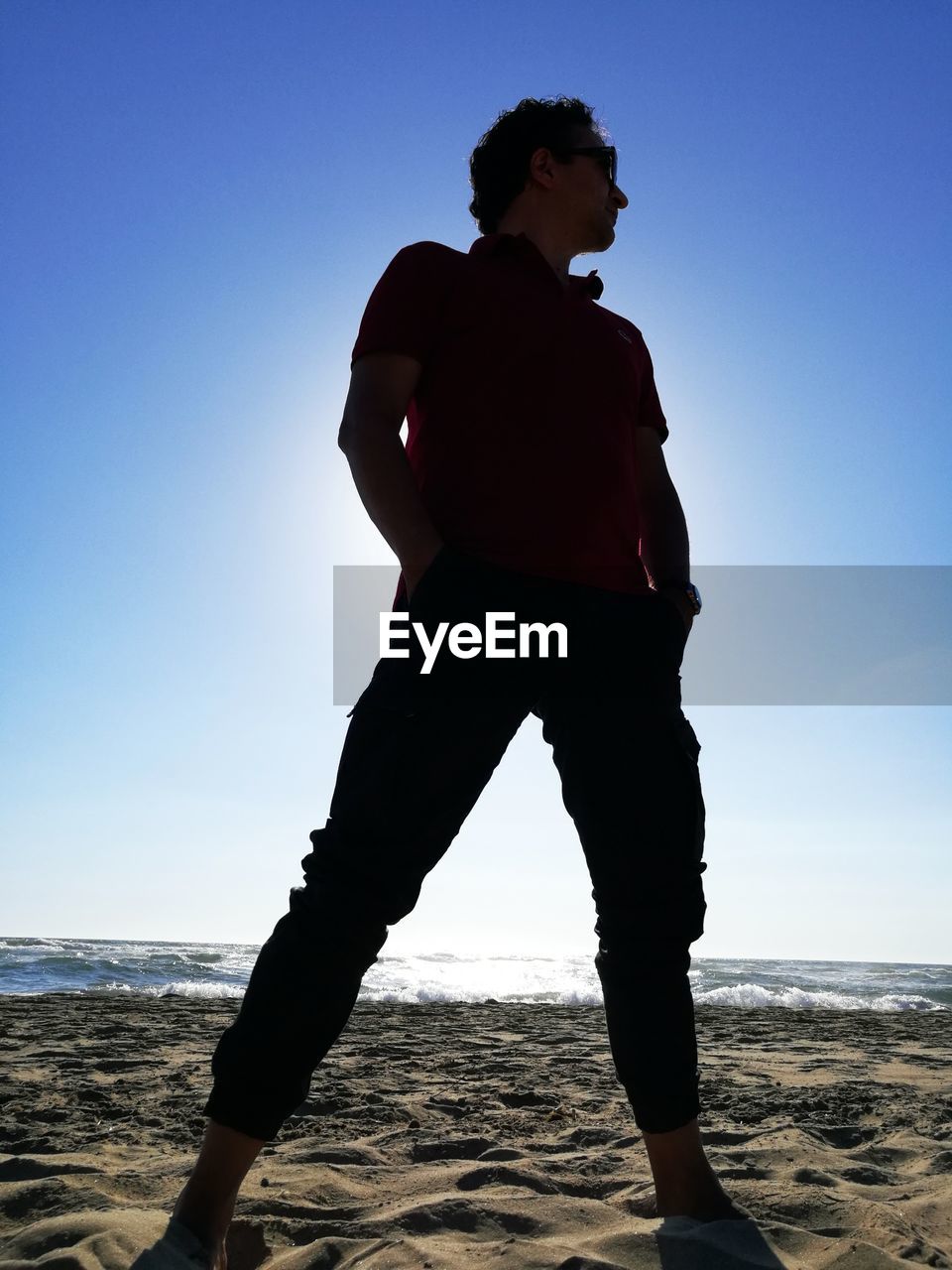 YOUNG MAN STANDING ON BEACH AGAINST CLEAR SKY