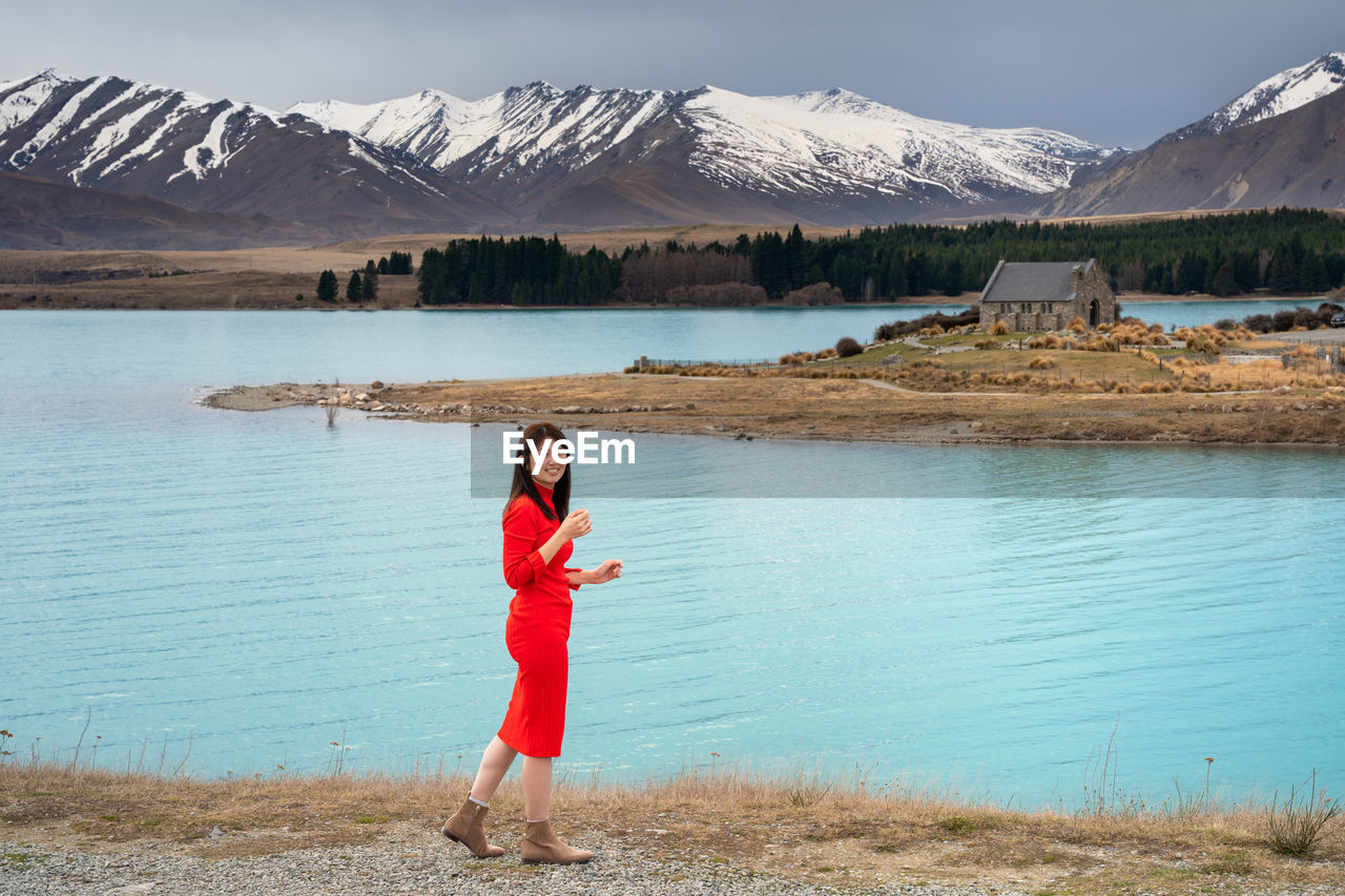 Asian female tourist pose at turquoise color lake tekapo with snowcapped mountain at the background